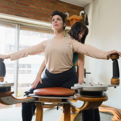 Female teacher teaching her female student correct technique of exercising on rehabilitation machine to strengthen and improve joint health.